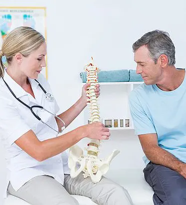 Chiropractor holding a spinal column demo with patient, spinal column example, chiropractor plano tx